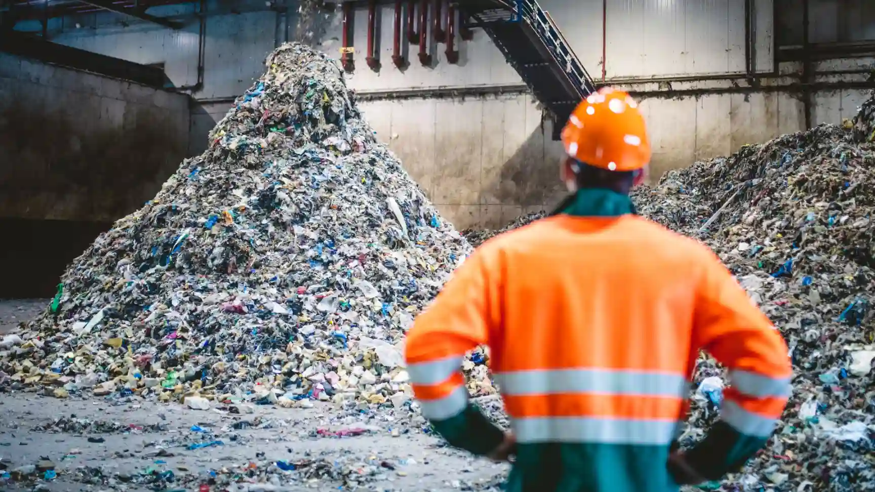 Operário de usina de tratamento de resíduos sólidos observando grande pilha de lixo plástico
