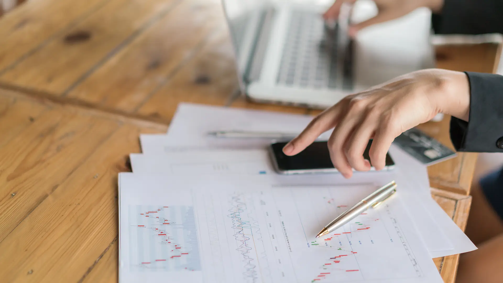 Pessoa analisando gráficos ambientais em uma mesa de trabalho, utilizando laptop, smartphone e documentos, focada em análise de regularizações ambientais de empresas.