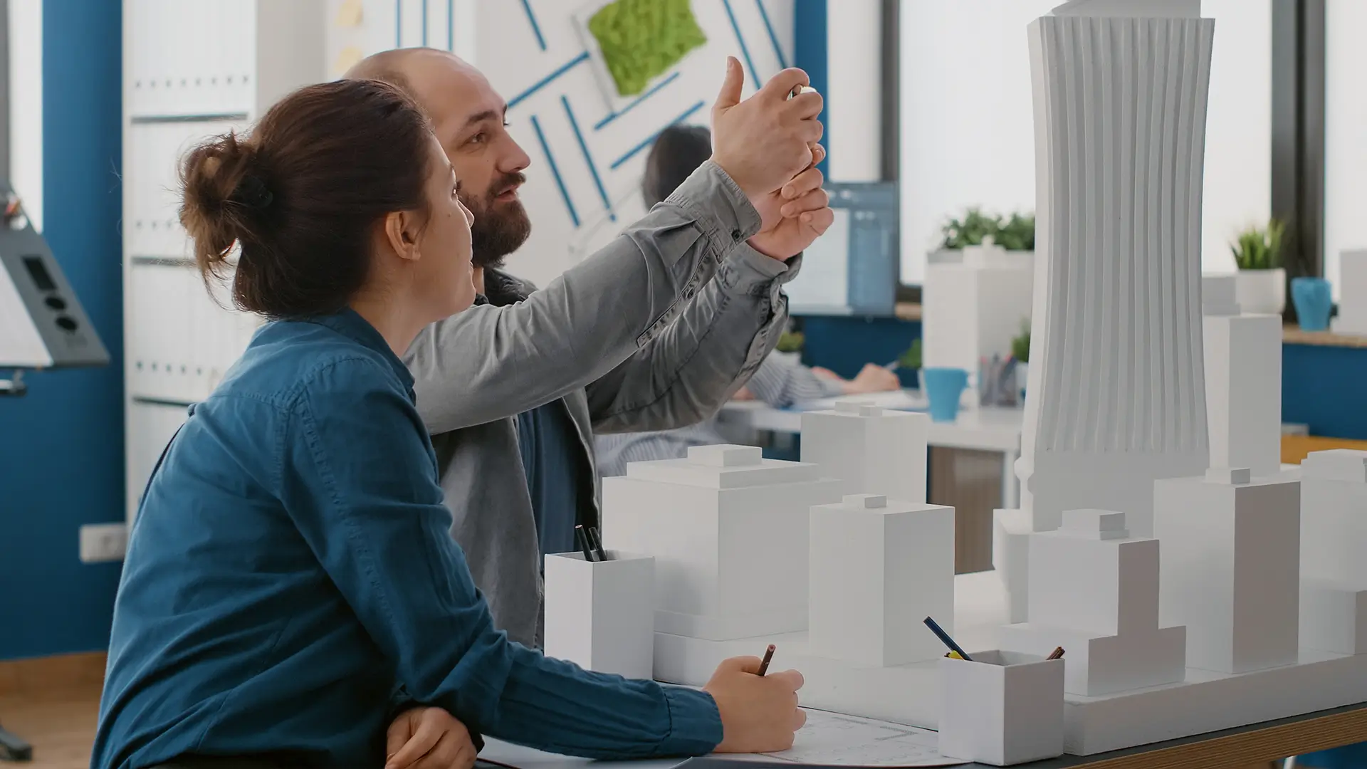 Engenheiros analisando um projeto arquitetônico de um edifício alto em uma sala de escritório moderna, com maquetes e gráficos ao fundo, discutindo planos de construção.