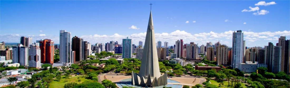 Vista panorâmica da cidade de Maringá com muitos edifícios altos, uma praça com espaço verde e uma igreja com torres pontiagudas ao centro